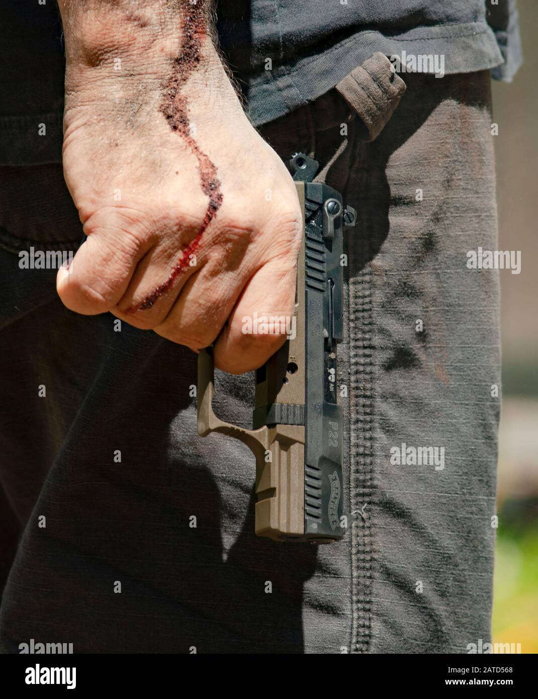 Man with dried blood on his hand and arm wearing tactical pants a holding Walther P22 automatic pistol. Stock Photo