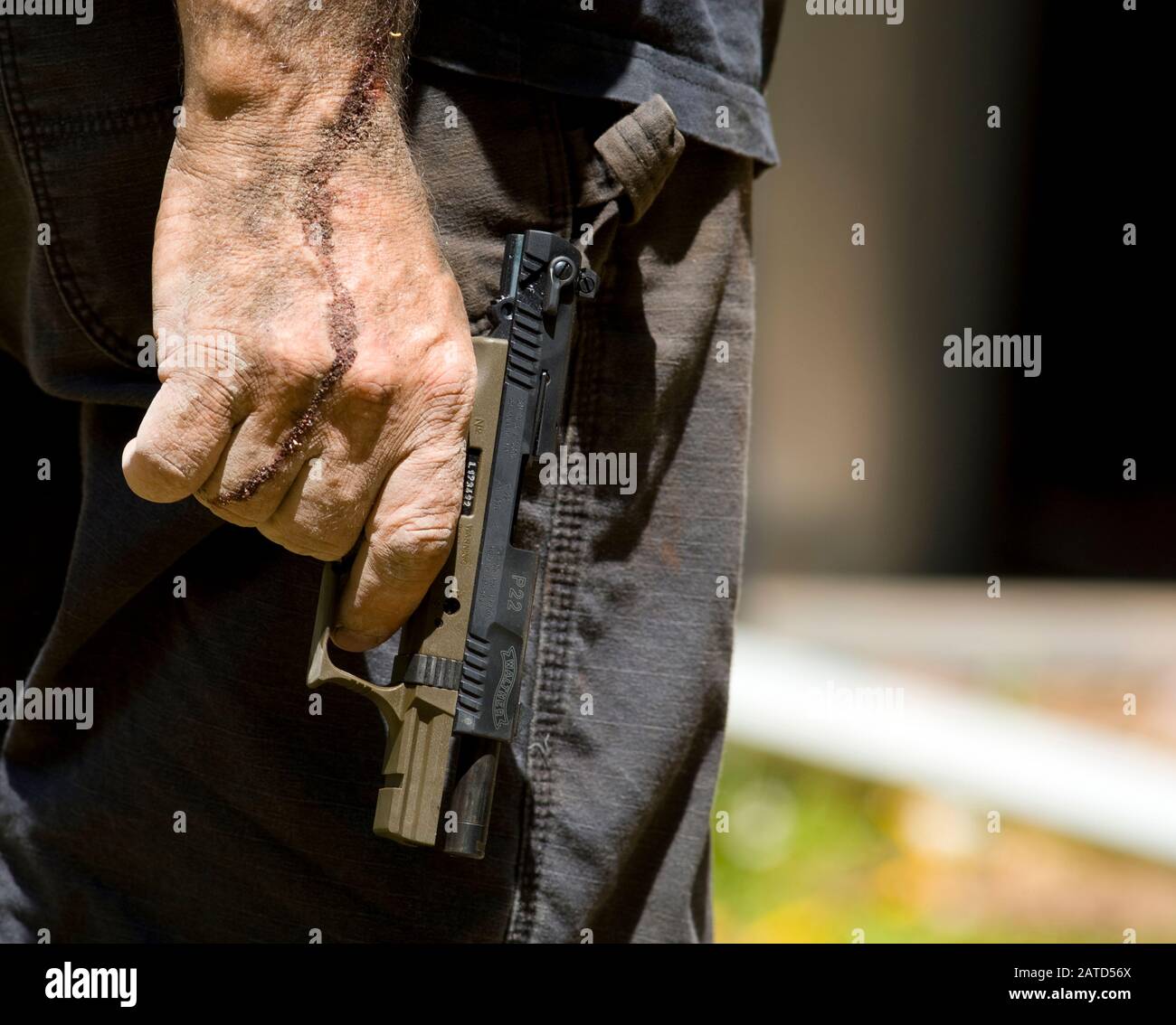 Man with dried blood on his hand and arm wearing tactical pants a holding Walther P22 automatic pistol. Stock Photo