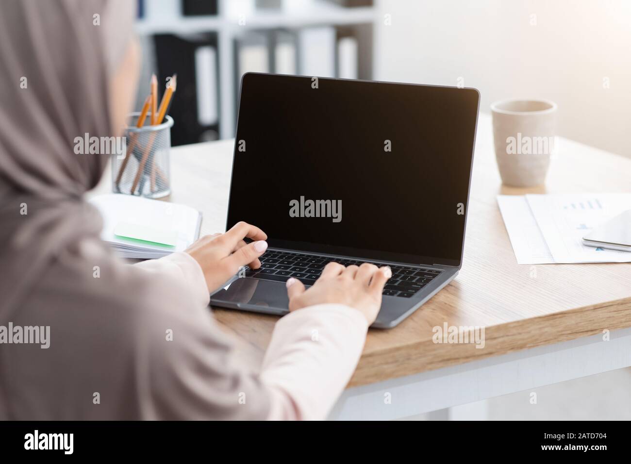 Muslim woman working on laptop with black screen, over shoulder view ...