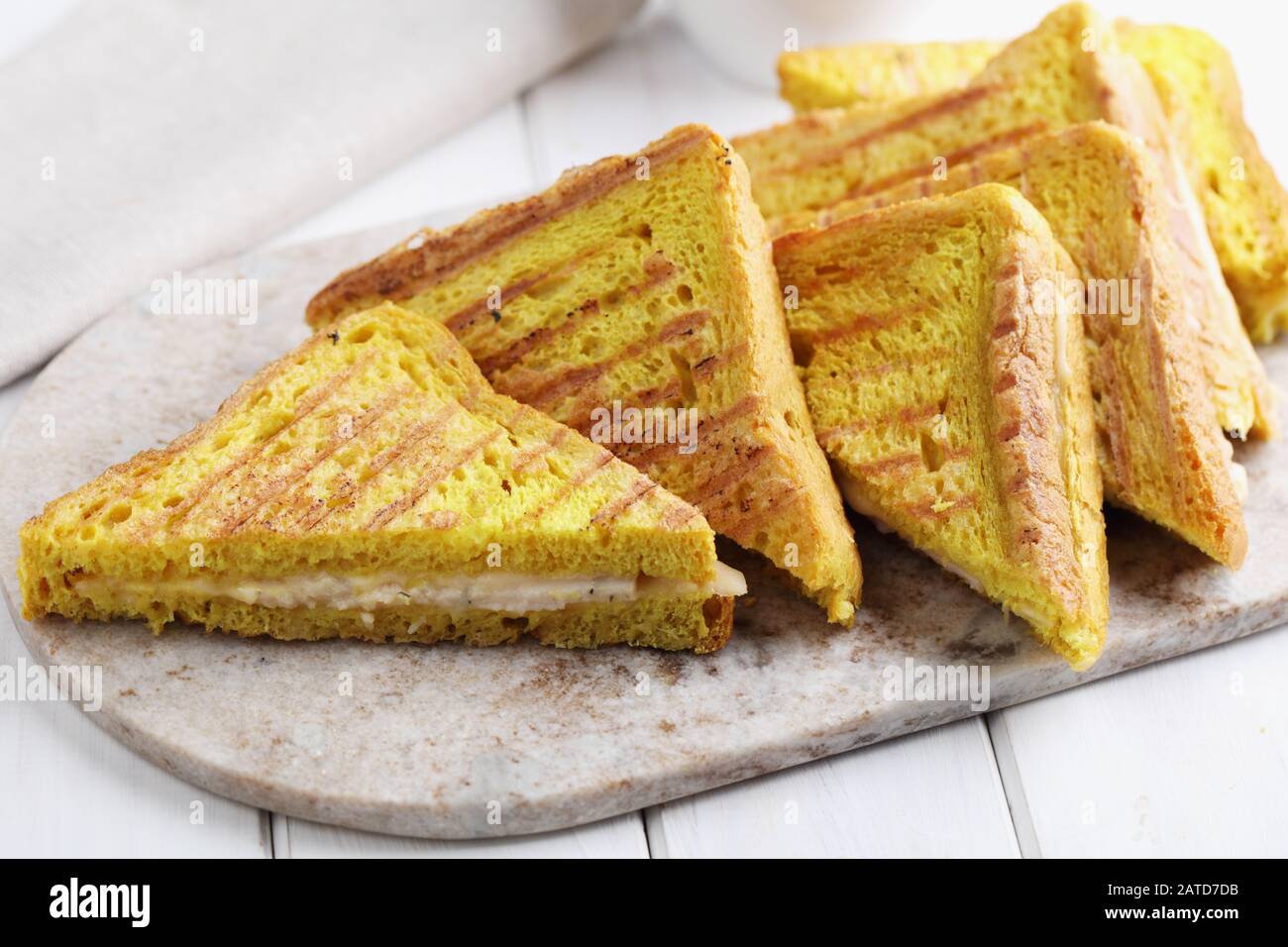 Grilled sandwiches with ham and cheese on a marble cutting board. Toast bread with curcuma gives a bright yellow color Stock Photo