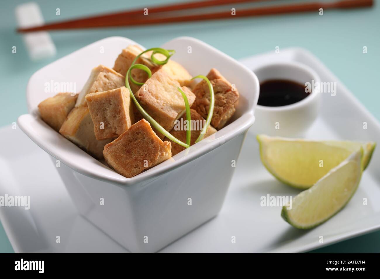 Fried tofu served with soy sauce, slices of lime, and green onion on a white plate closeup Stock Photo