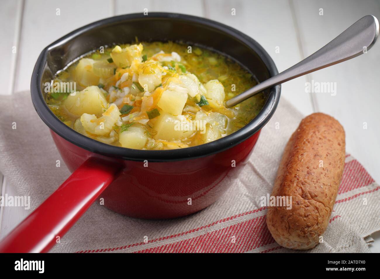 Vegan soup with potato, celery, carrot, rice, and green onion in a red saucepan Stock Photo