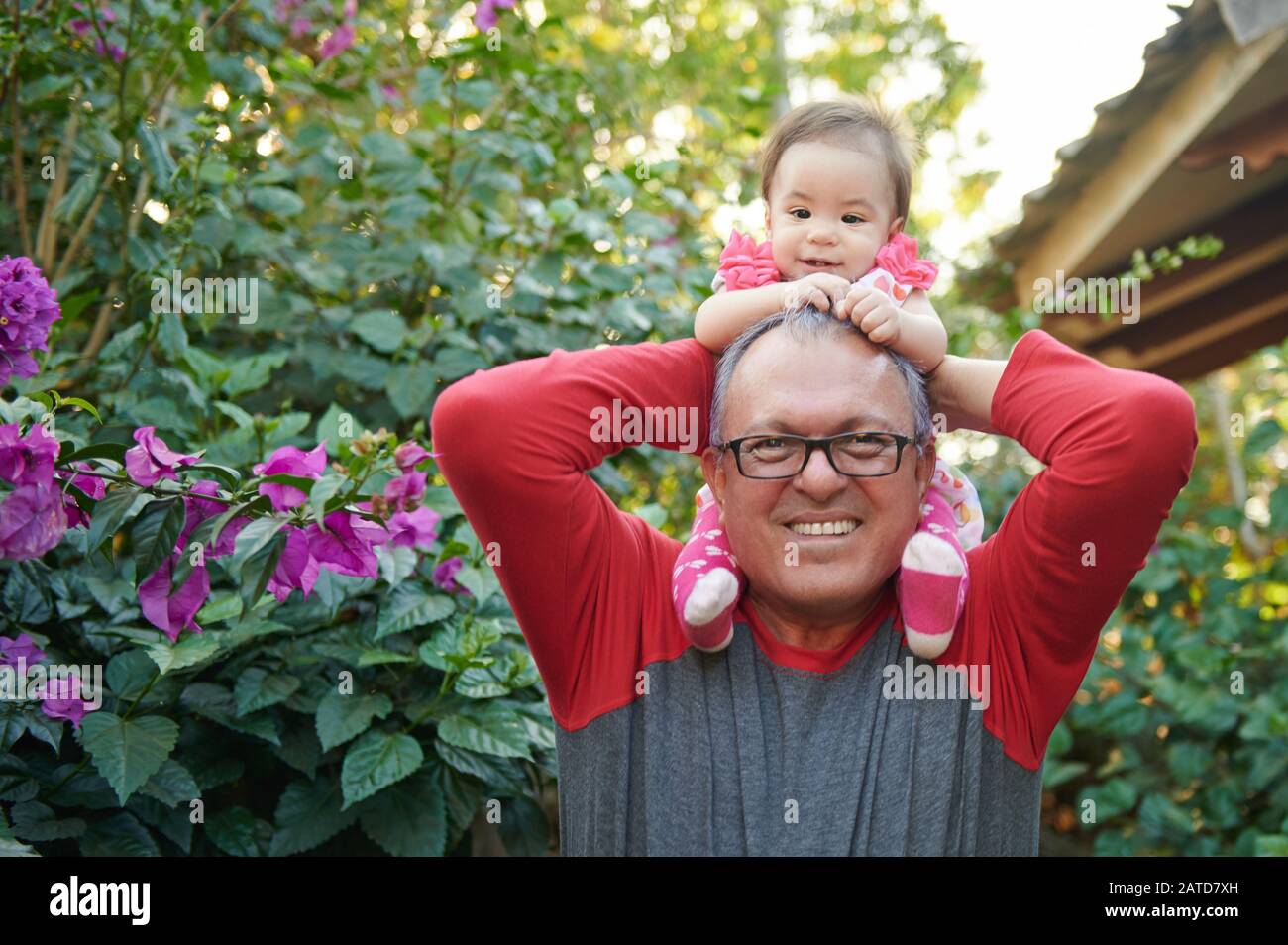 Happy smiling grandpa hold baby girl on shoulders on sunny park background Stock Photo
