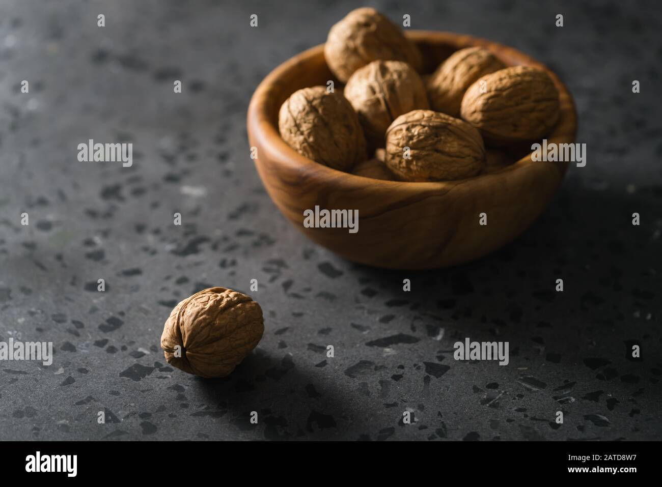 inshell walnuts in olive wood bowl on terrazzo countertop, shallow focus Stock Photo
