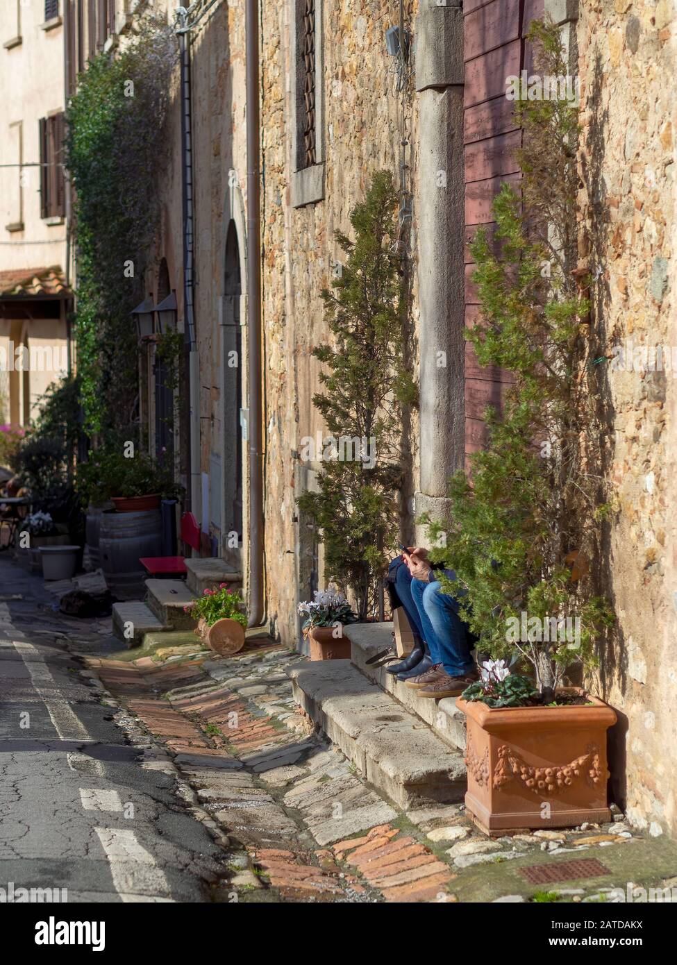 Two unidentifiable tourists on mobile phones in scenic Italian village of Bolgheri, Tuscany. Modern life concept. Only knees visible. Stock Photo