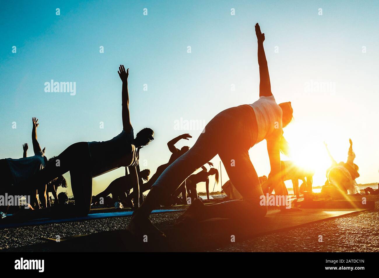 Silhouette of men and women doing yoga outdoor - Group of people doing meditation at sunset - Spiritual concept for healthy and relaxing lifestyle - F Stock Photo