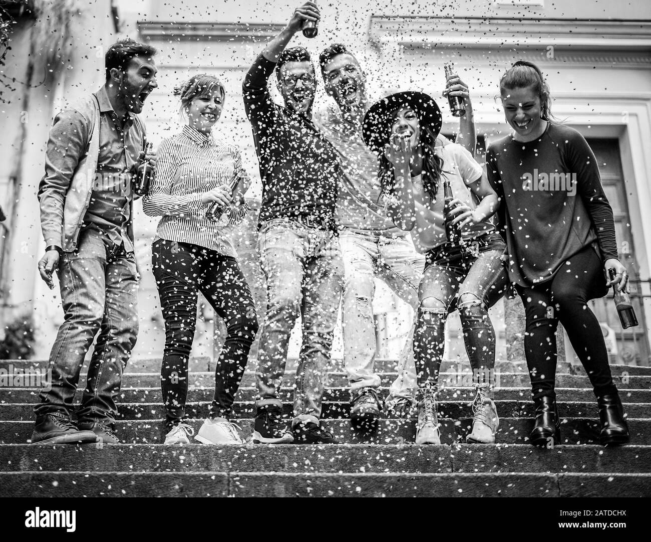 Group of friends making party outdoor with confetti and beers - Young people drinking alcohol and having fun on the street - Black and white editing - Stock Photo