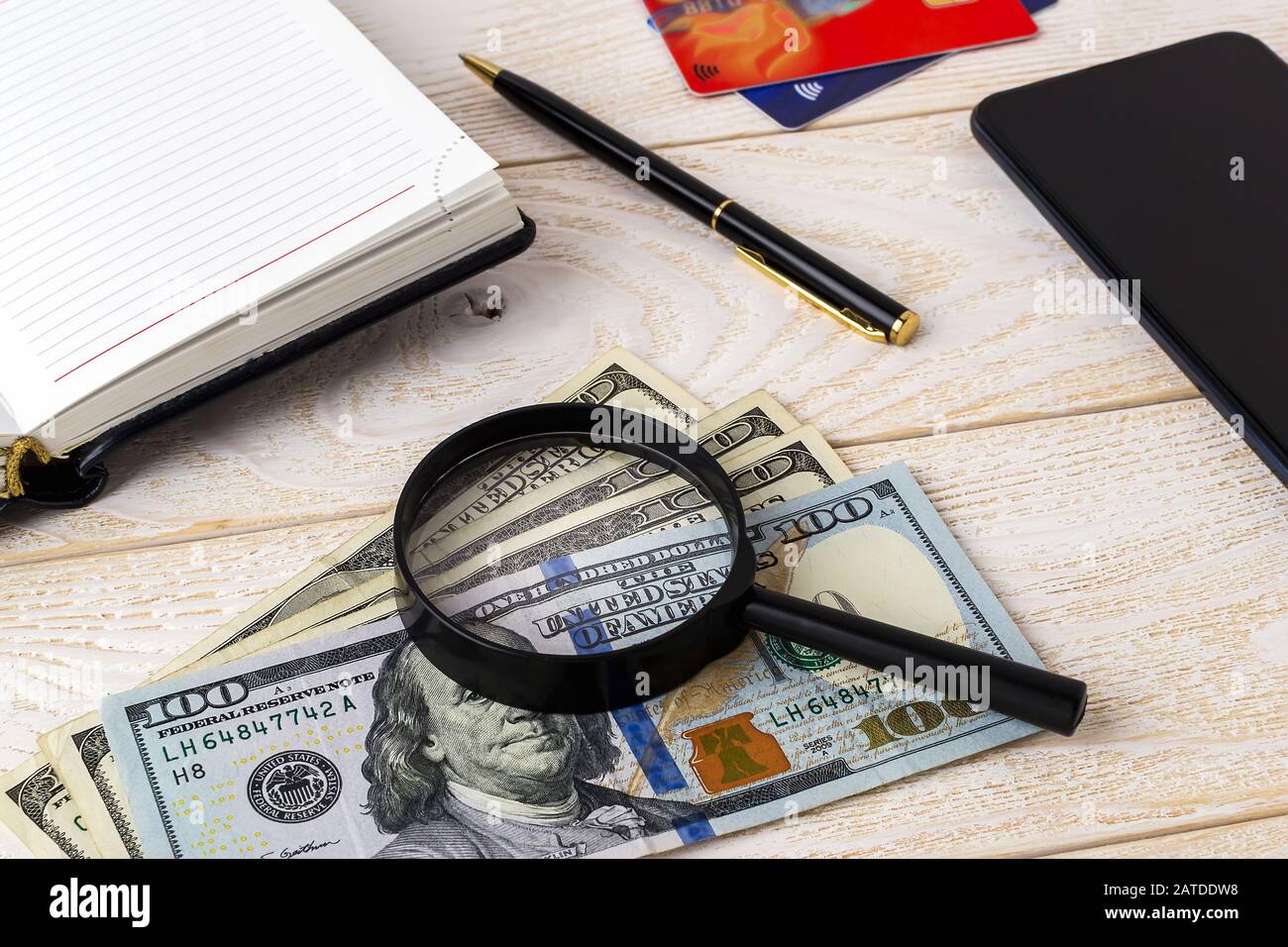Magnifier on dollar banknotes near pen, note book, credit cards and