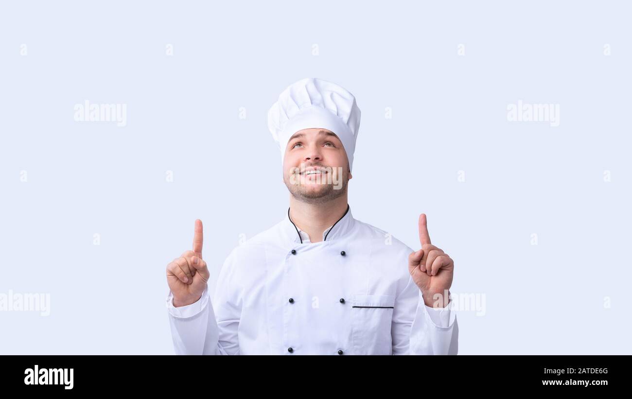 Chef Guy Pointing Fingers Upward Standing Over White Background, Panorama Stock Photo