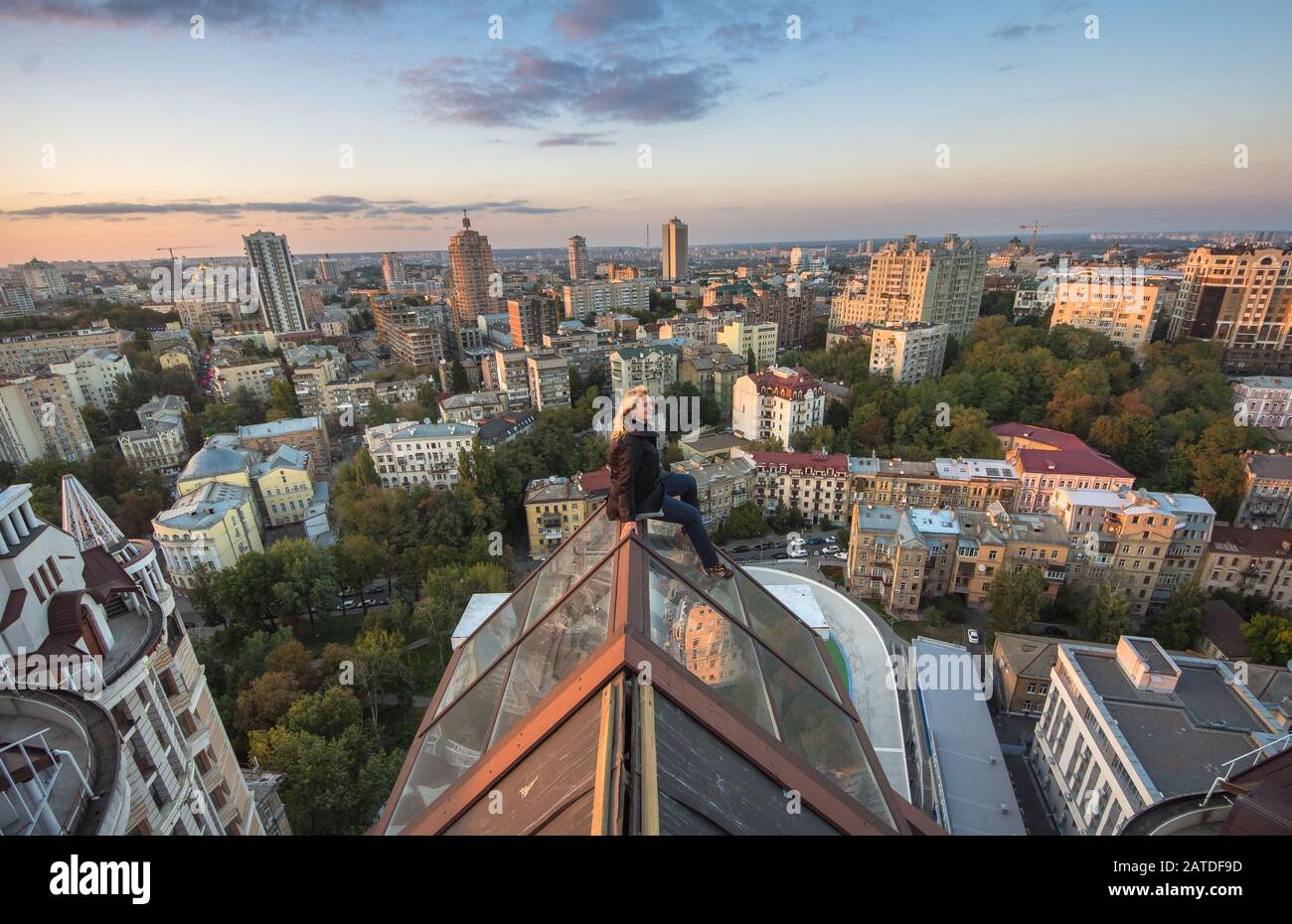 Woman seatting on the roof on the modern building in Kiev, Ukraine. Extreme  girl climbing on the rooftop in Kiev city. Sunset time on the roofs in Kie  Stock Photo - Alamy