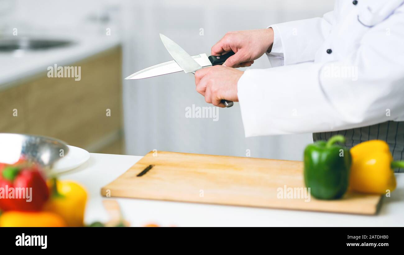 Unrecognizable Cook Guy Sharpening Knives In Restaurant Kitchen, Panorama, Cropped Stock Photo