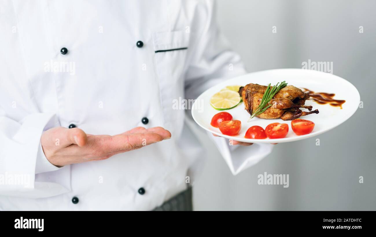 Unrecognizable Chef Holding Plate With Roasted Chicken Standing In Kitchen Stock Photo