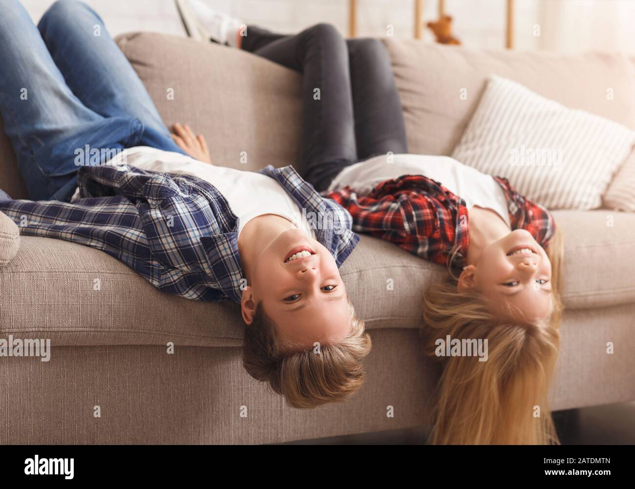 Brother And Sister Sitting On Couch Upside Down At Home Stock Photo
