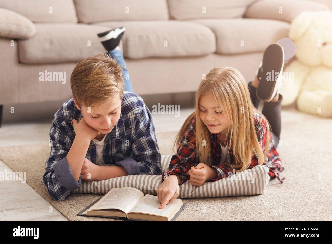 Brother And Sister Reading Book Lying On Floor At Home Stock Photo