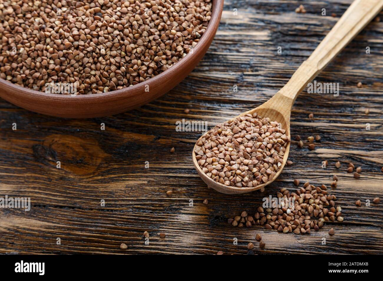 raw buckwheat in a clay plate on a wooden background. view from above. nearby lies a spoon. place for text Stock Photo
