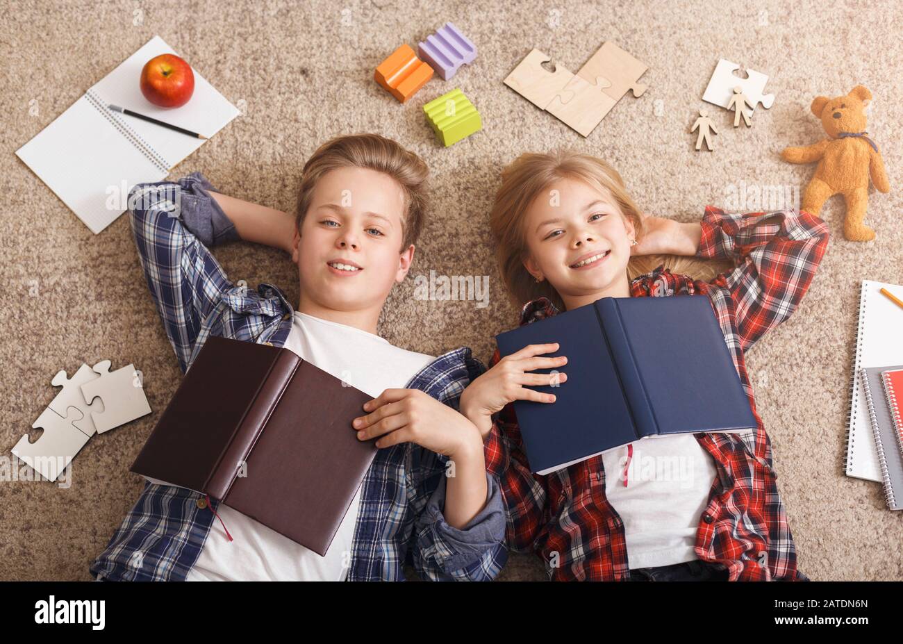 Siblings Lying On Floor Doing Homework Posing At Home, Top-View Stock Photo