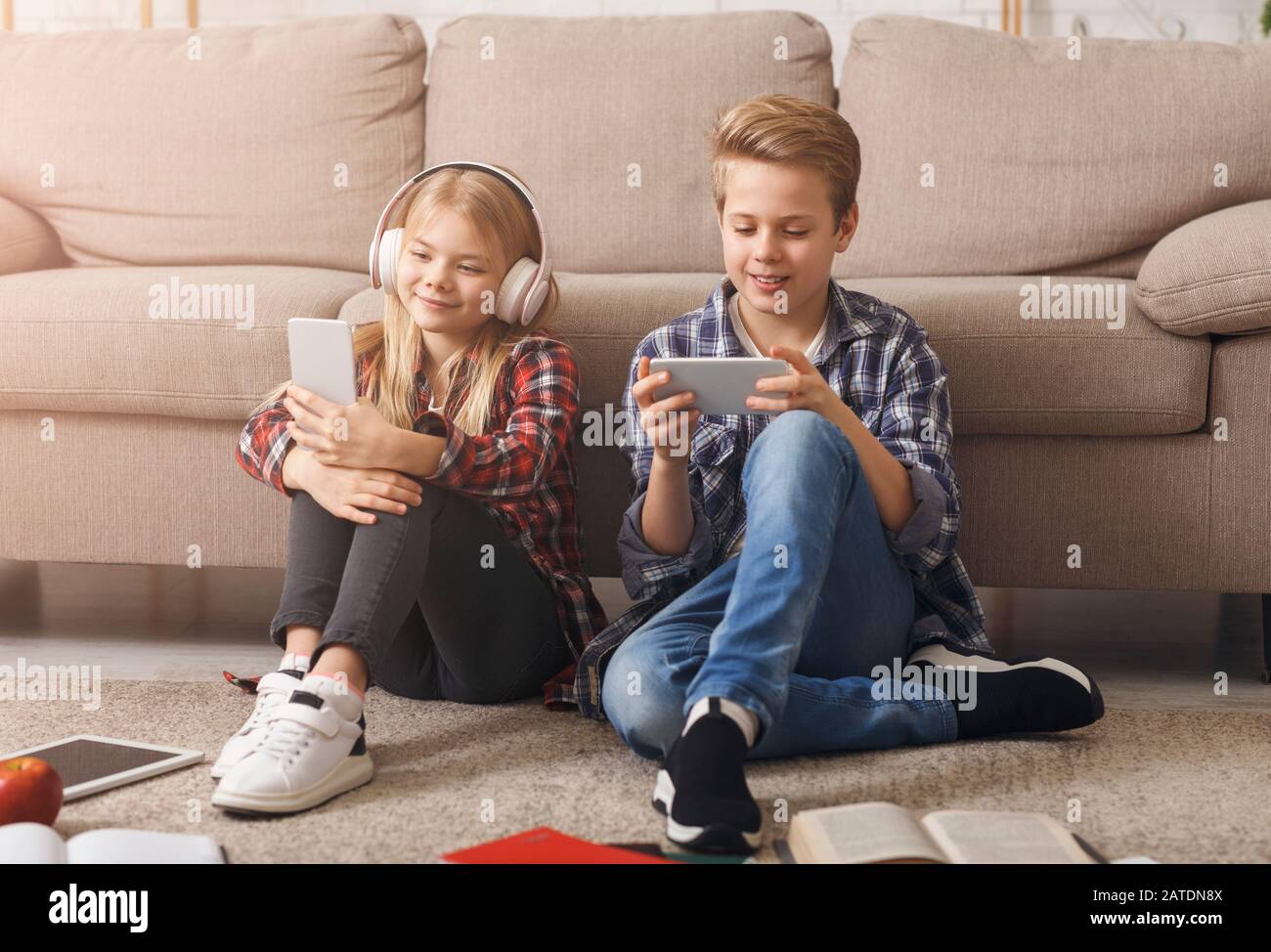 Brother And Sister Using Smartphones Sitting On Floor Indoor Stock Photo