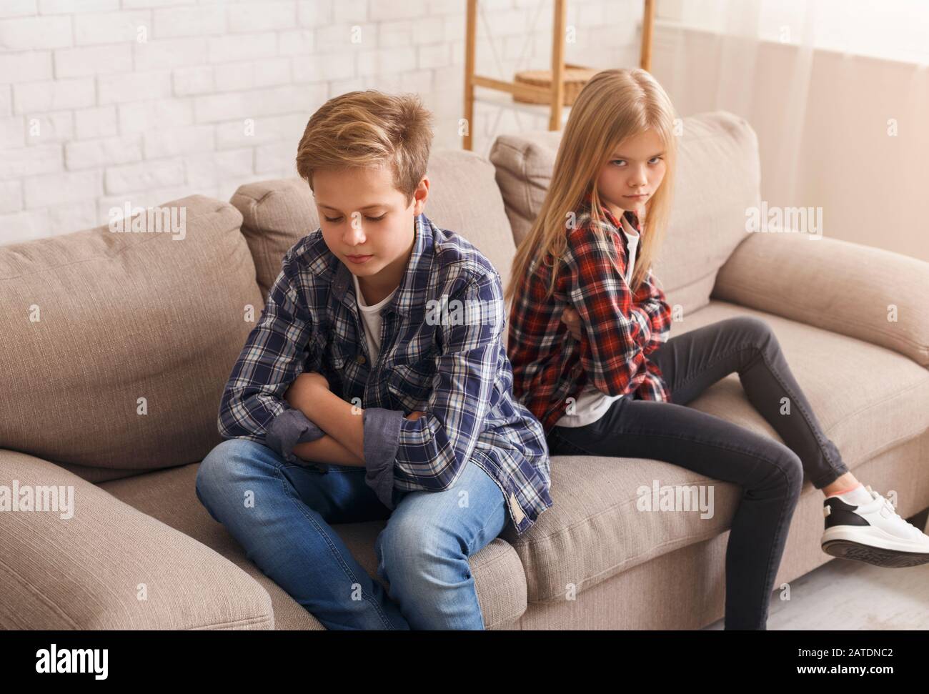 Siblings After Quarrel Sitting Back-To-Back On Couch At Home Stock Photo