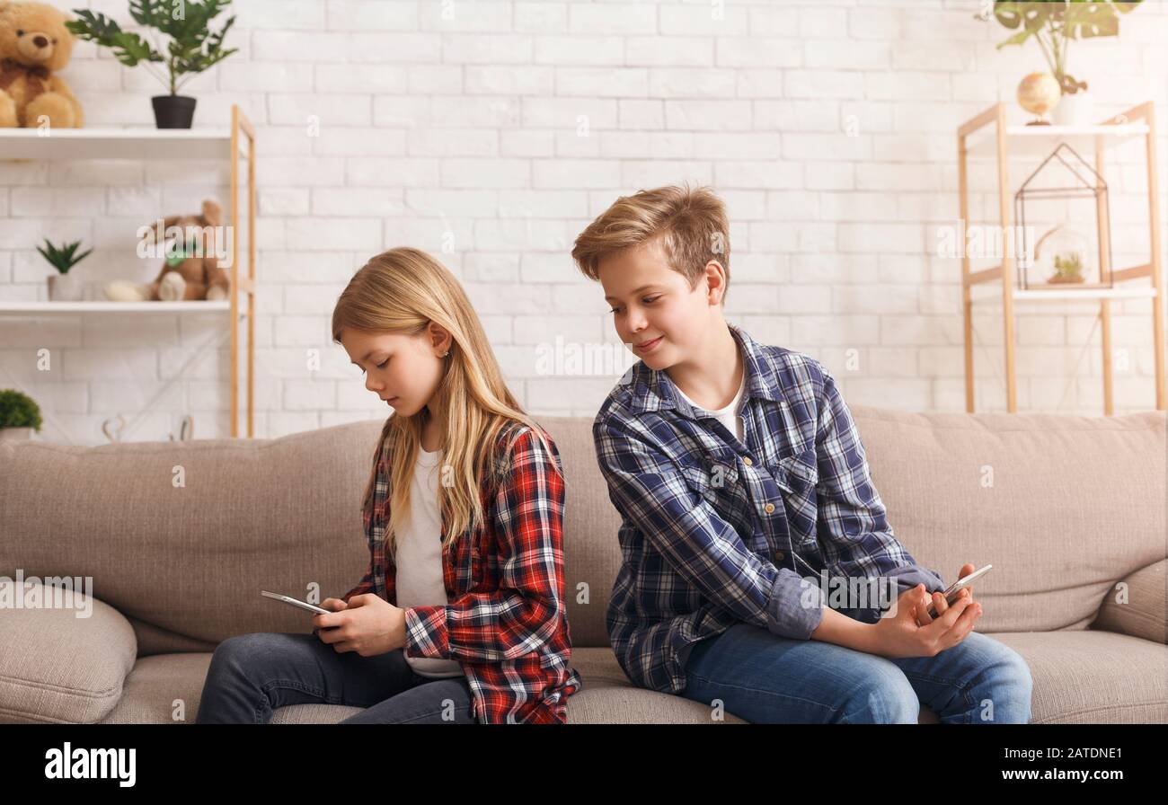Curious Brother Reading Sister's Messages On Phone Sitting On Couch Stock Photo