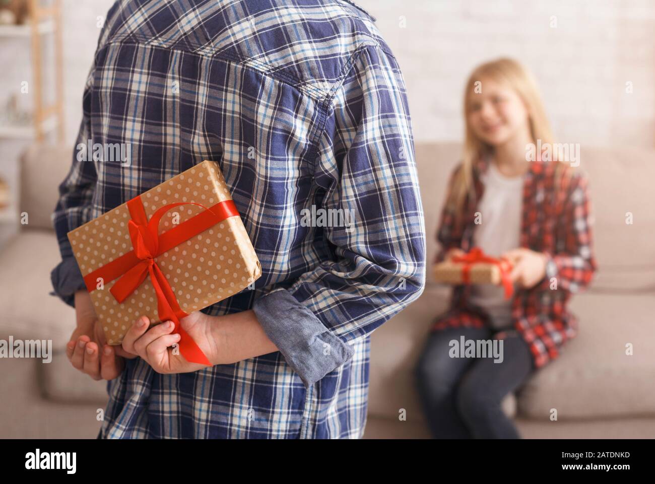 Unrecognizable Boy Holding Gift Congratulting Girl Sitting On Couch Indoor Stock Photo
