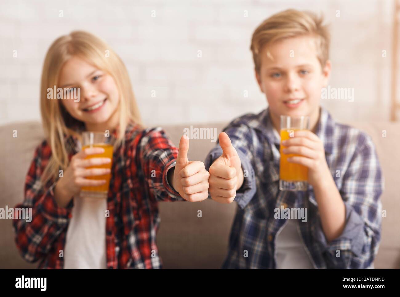 Boy And Girl Drinking Juice Gesturing Thumbs-Up Sitting On Sofa Stock Photo