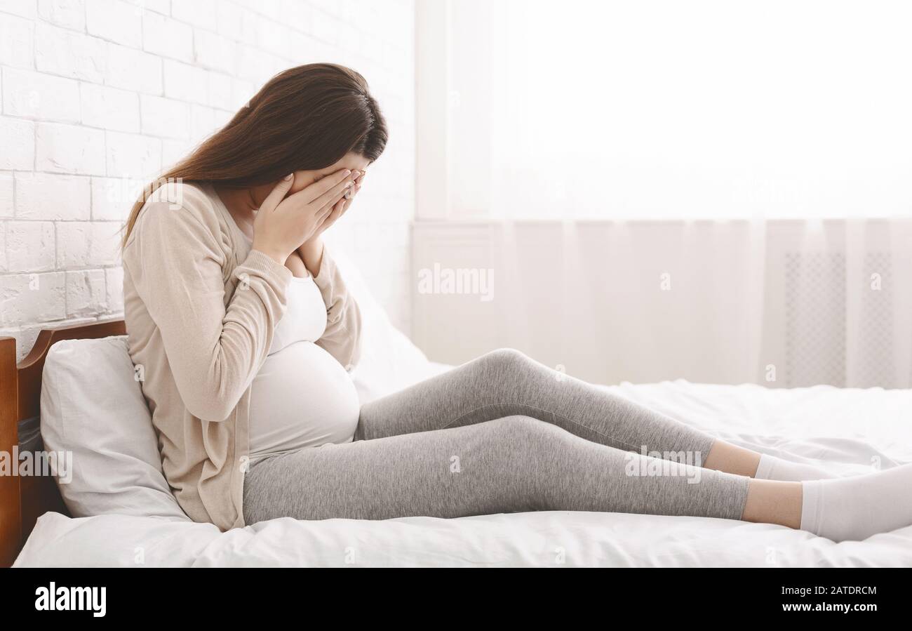 Young pregnant woman feeling sad and crying at home Stock Photo