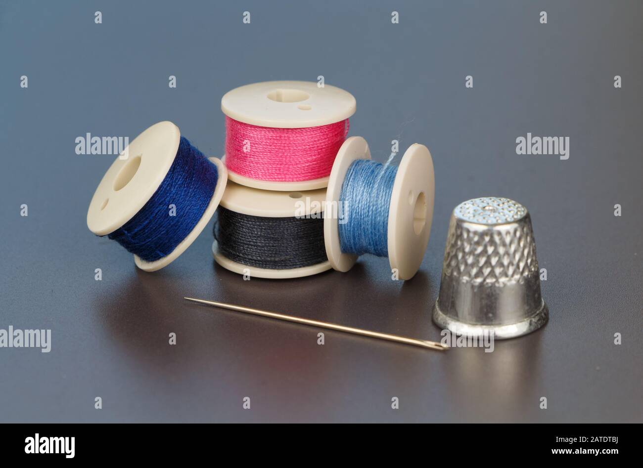 Blue, gray and pink reels of thread for sewing, needle and thimble Stock Photo