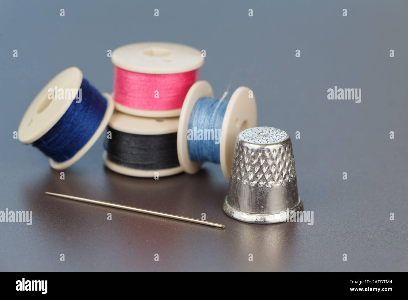 Reel of blue, pink and gray thread for sewing, needle and thimble Stock Photo