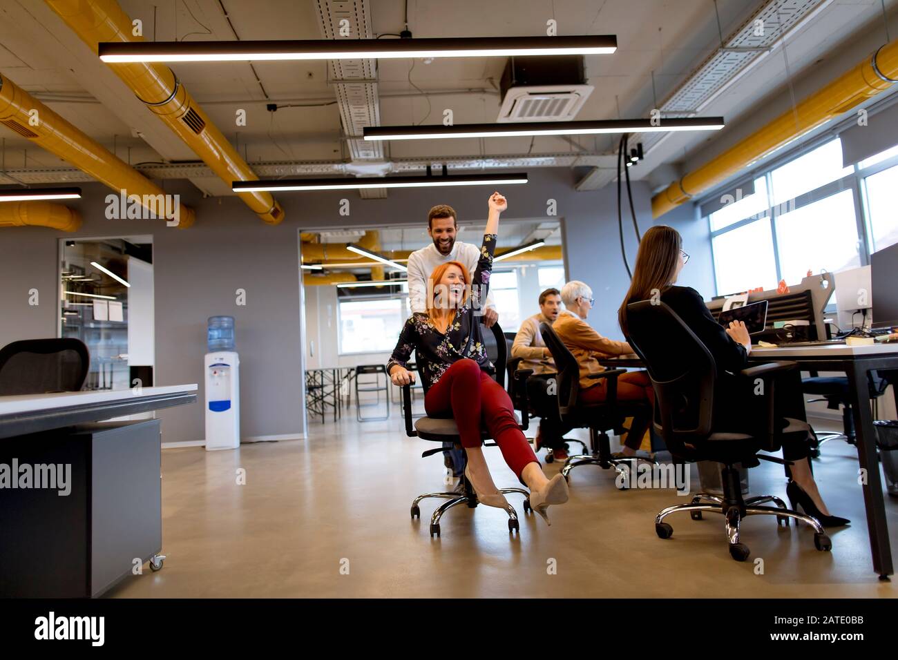 Young cheerful business people in smart casual wear having fun while racing on office chairs and smiling Stock Photo