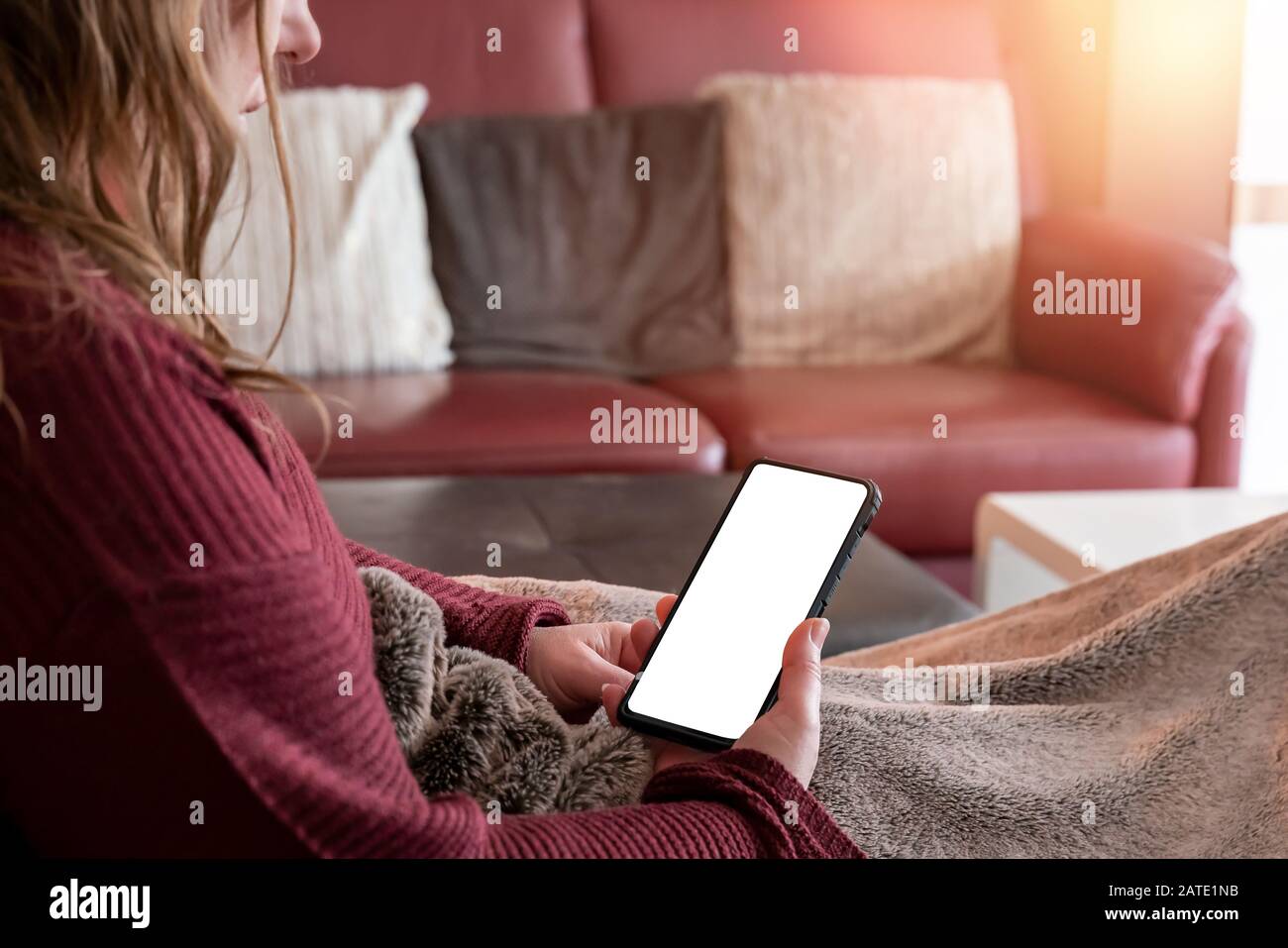 A middle-aged woman is lying on the couch at home. She looks at smartphone. Copy space for your own designs. Red ambience. Stock Photo