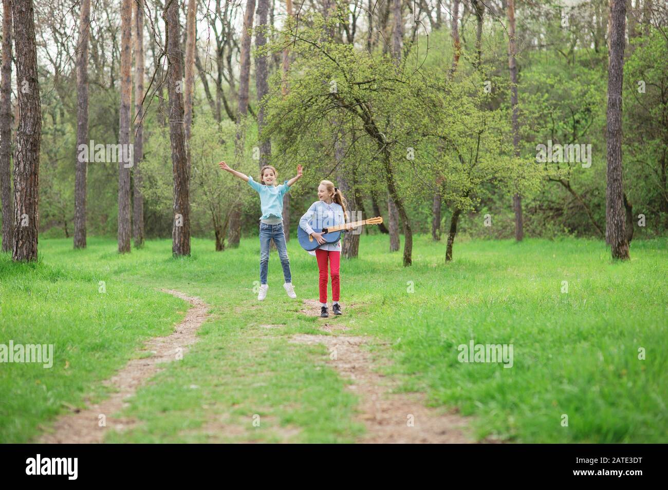 two active happy girls jumping and playing music on guitar and singing song in outdoor spring park Stock Photo