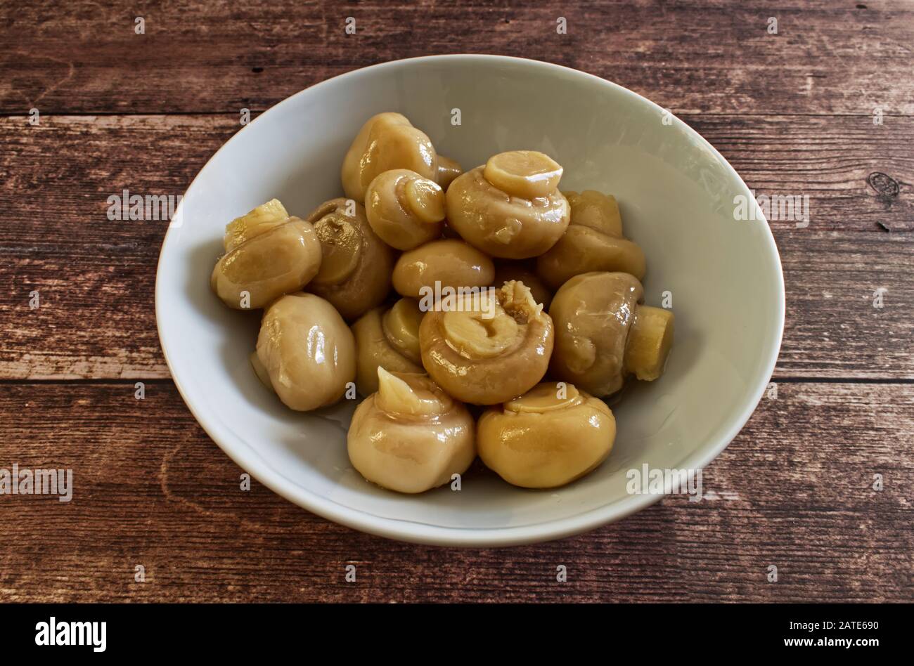 Pickled white mushrooms in white bowl on wooden table Stock Photo