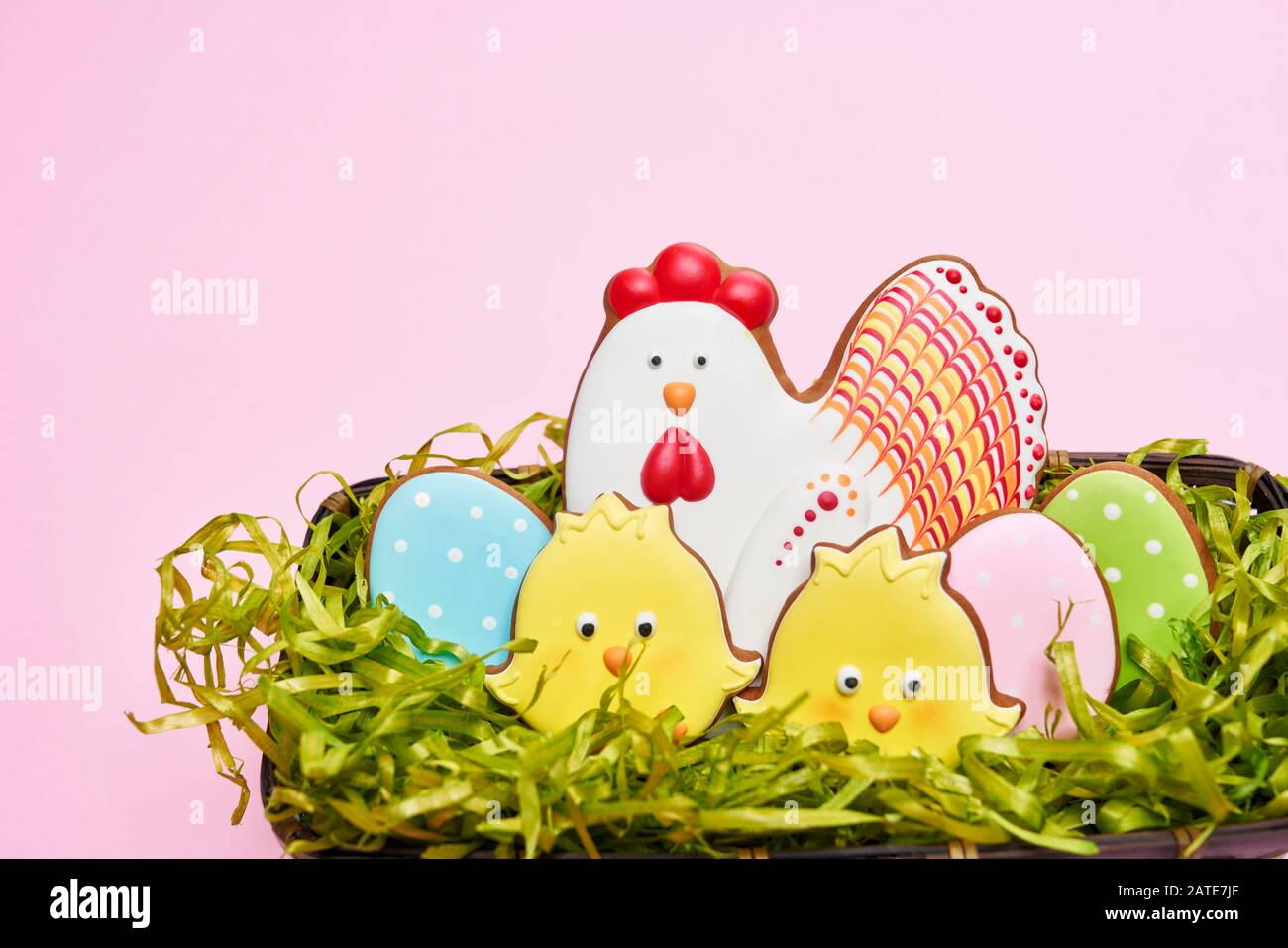 From above view of glazed cookies in shape of lovely yellow chicks, chicken and colorful eggs lying in box with fake green grass isolated on pink background. Spring and easter holidays concept. Stock Photo