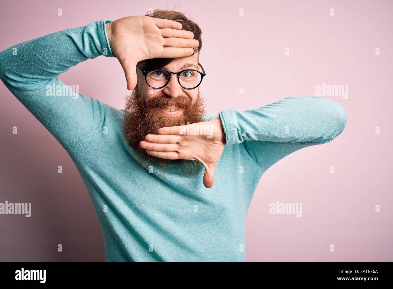 Handsome Irish redhead man with beard wearing glasses over pink ...