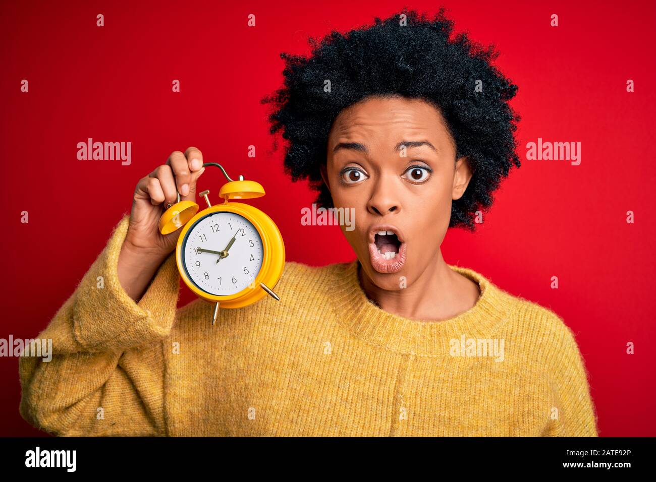 Young African American afro woman with curly hair holding vintage alarm