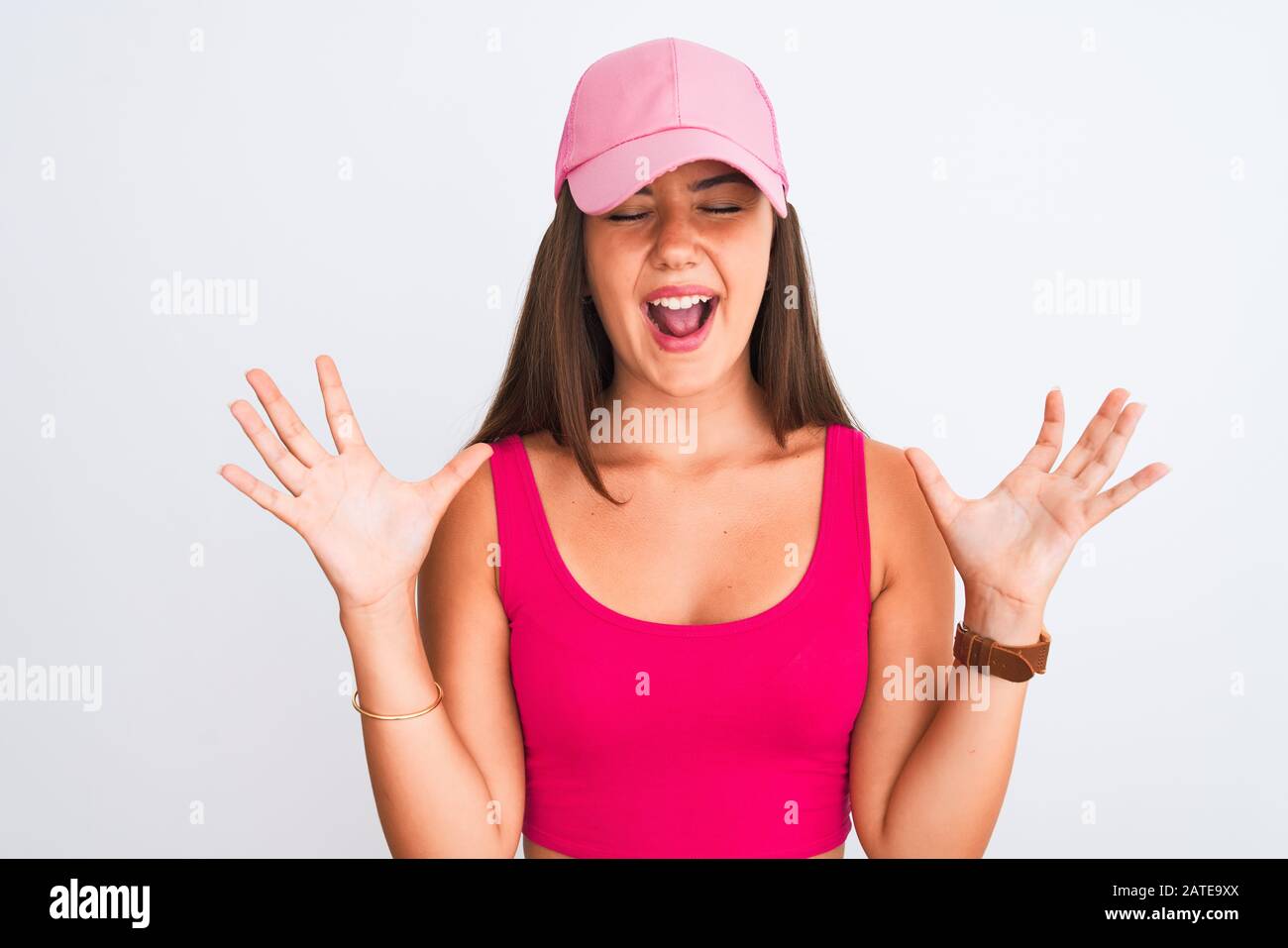 Young beautiful girl wearing pink casual t-shirt and cap over isolated white background celebrating mad and crazy for success with arms raised and clo Stock Photo