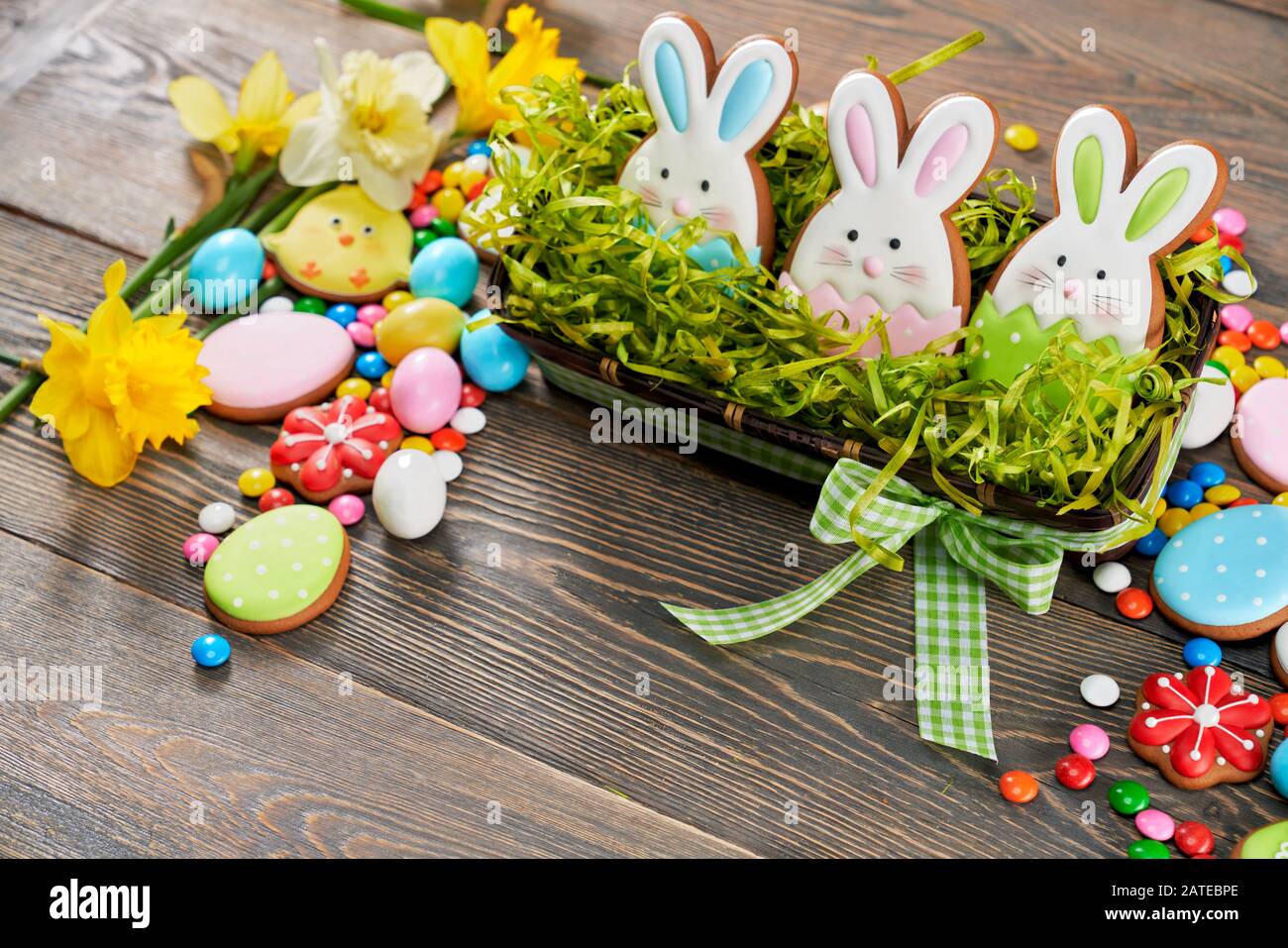 Selective focus of easter ginger glazed cookies in shape of animals, eggs, three bunnies in box with fake grass, daffodils isolated on wooden background. Peanut chocolate balls in sugar shell Stock Photo - Selective focus of easter ginger glazed cookies in shape of animals, eggs, three bunnies in box with fake grass, daffodils isolated on wooden background. Peanut chocolate balls in sugar shell Stock Photo -