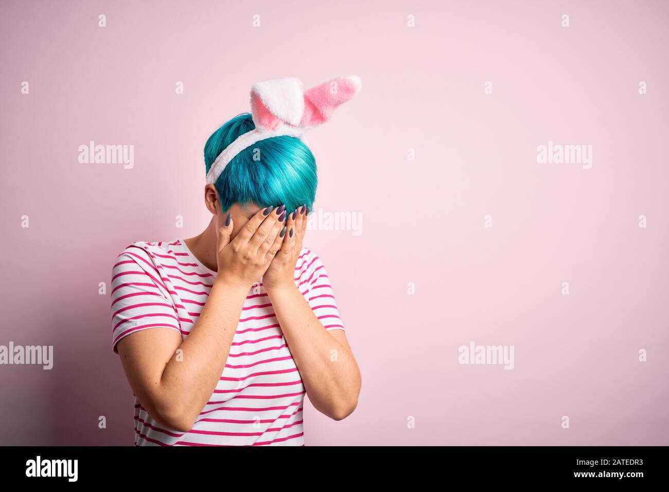Young woman with fashion blue hair wearing easter rabbit ears over pink ...
