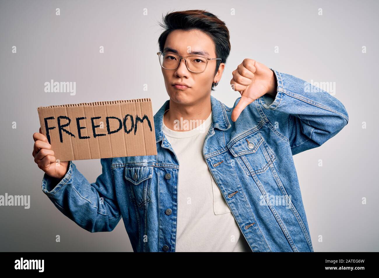Young handsome chinese activist man protesting asking for freedom holding poster with angry face, negative sign showing dislike with thumbs down, reje Stock Photo