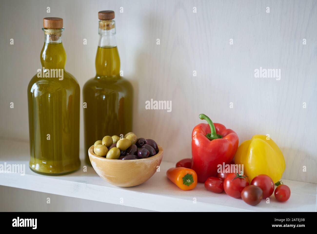 two wonderful bottles of cooking oil or olive oil on a wall shelf, wooden bowl with olives green and black next to vegan vegetarian vegetables Stock Photo