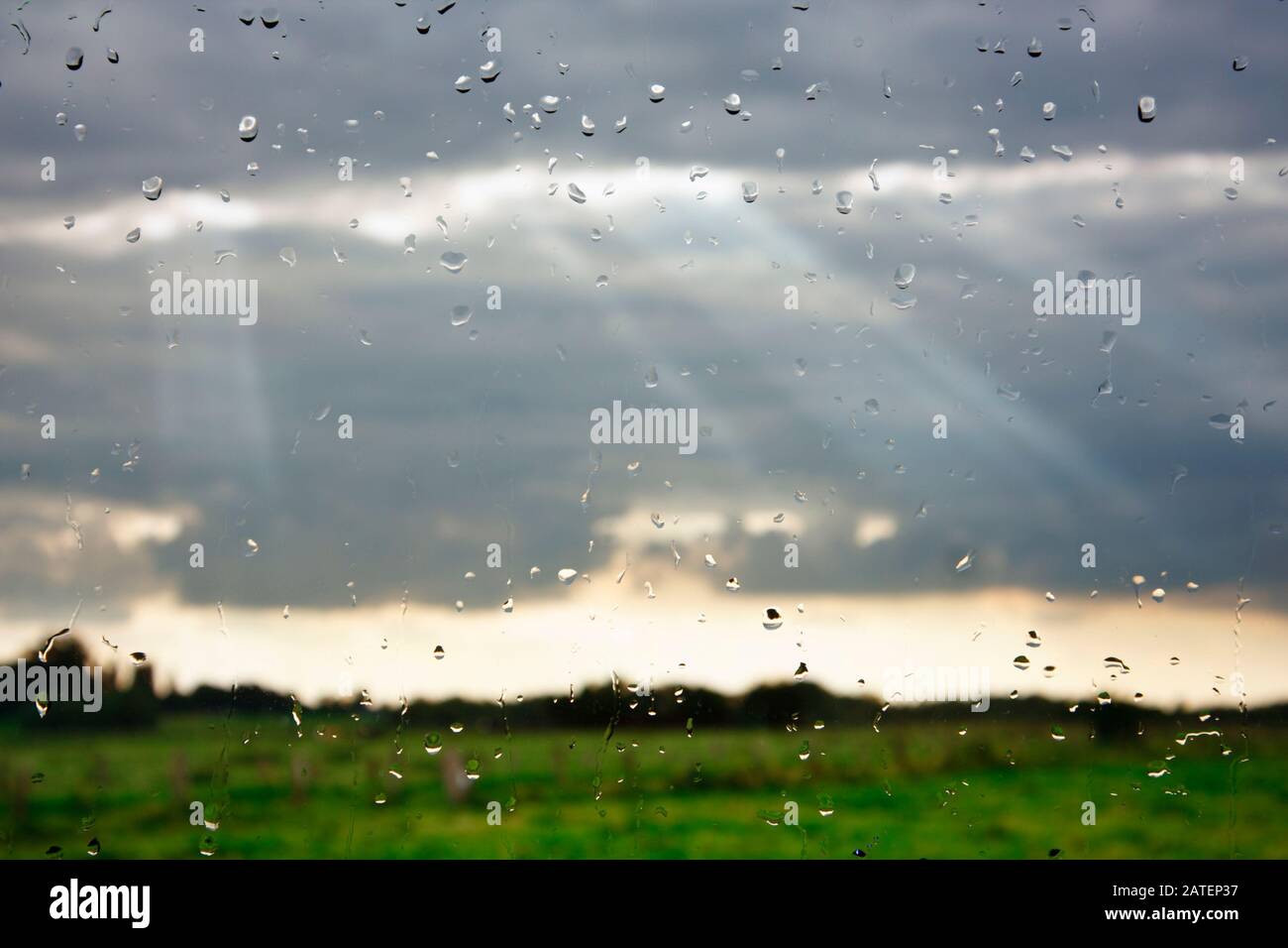 Sunbeams breaking through the clouds seen through a wet window. Stock Photo