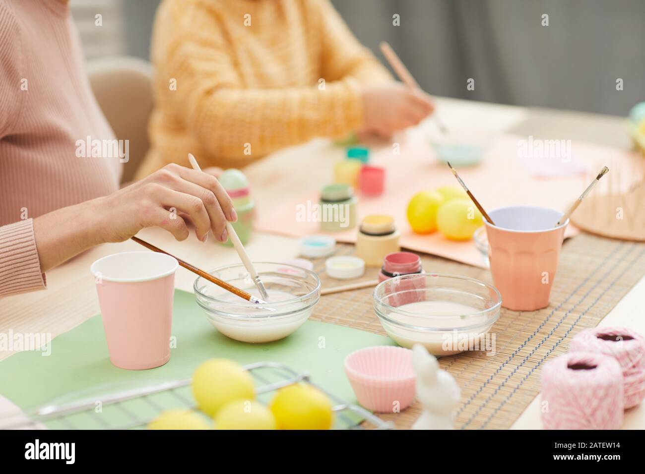 Close up of unrecognizable mother and daughter painting Easter eggs pastel colors sitting at table in cozy kitchen interior, copy space Stock Photo