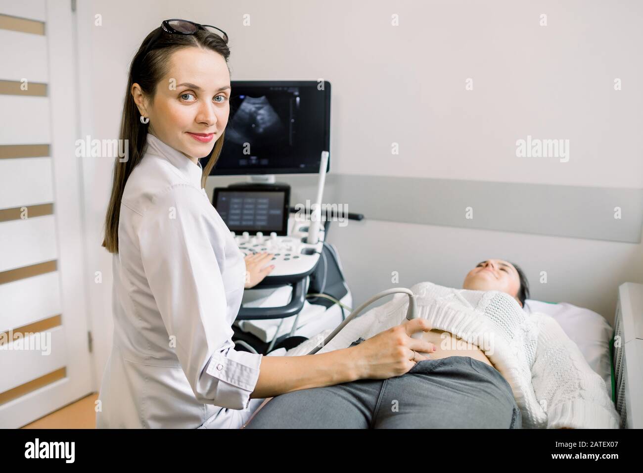 Pretty female doctor operating modern ultrasound scanner while examining belly and bladder of her female patient. Stock Photo