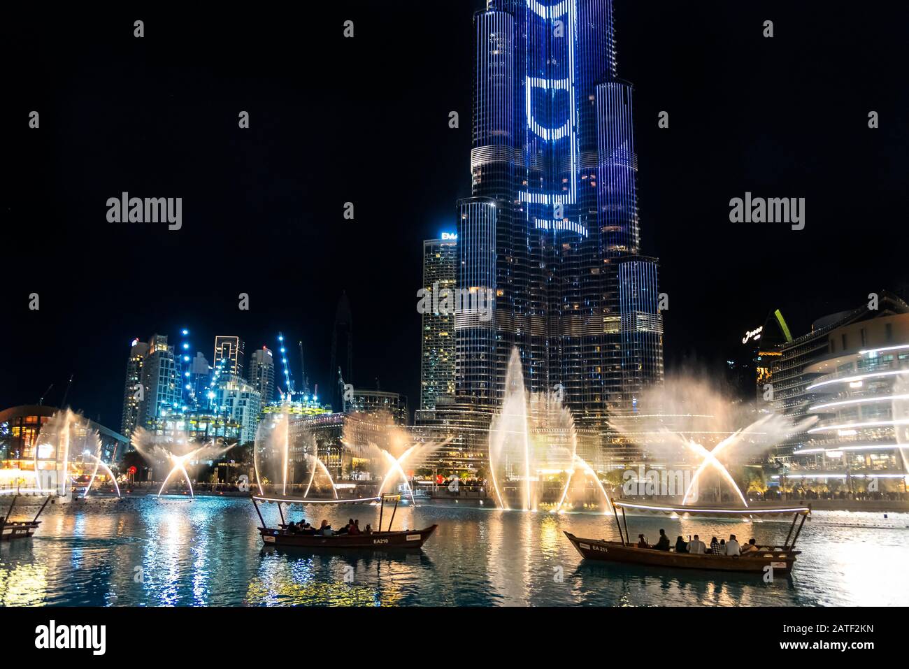 Tourist boats watching the choreographed fountain display at Dubai la Fontane at night reflected on the water in Burj Khalifa Lake Stock Photo