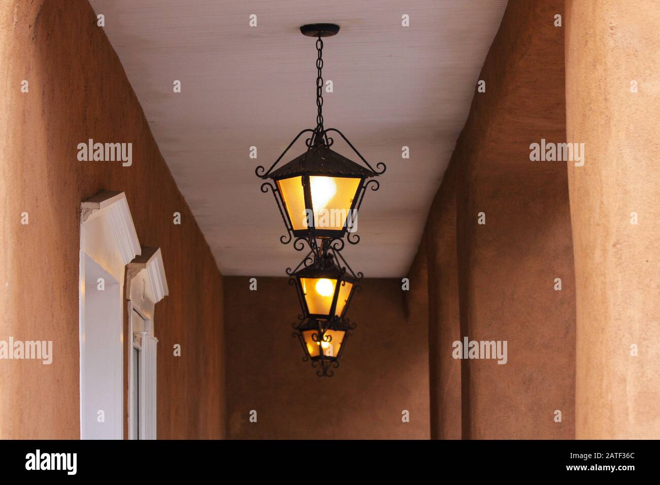 Three lantern lights in adobe building porch with plaster wall posts. Ornate iron lights white ceiling Stock Photo