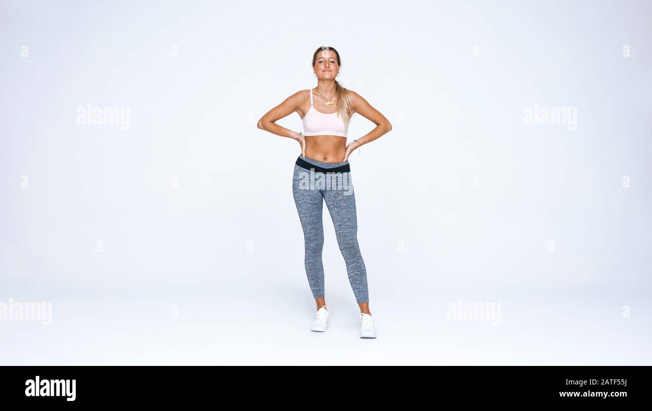 fitness woman standing against white background with her hands on waist. Female athlete in fitness clothes looking at camera. Stock Photo