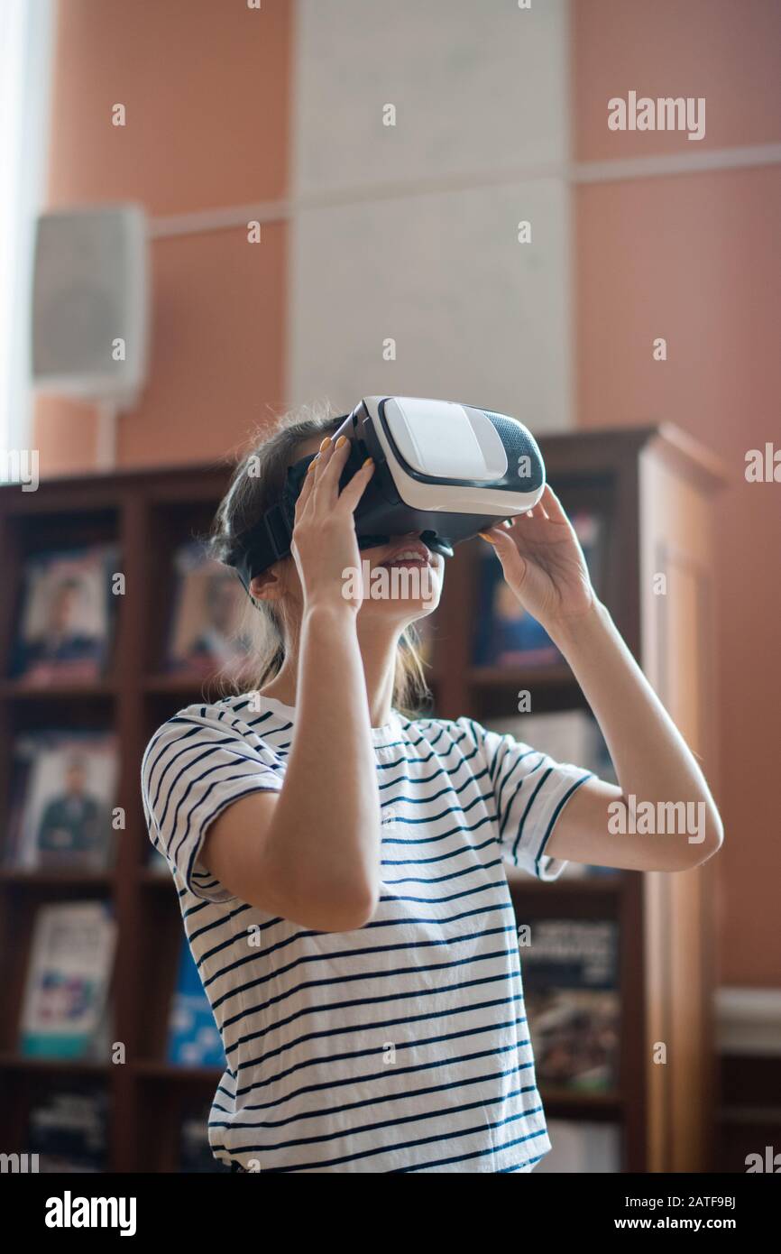 Contemporary teenage girl with vr headset watching 3d movie in library Stock Photo
