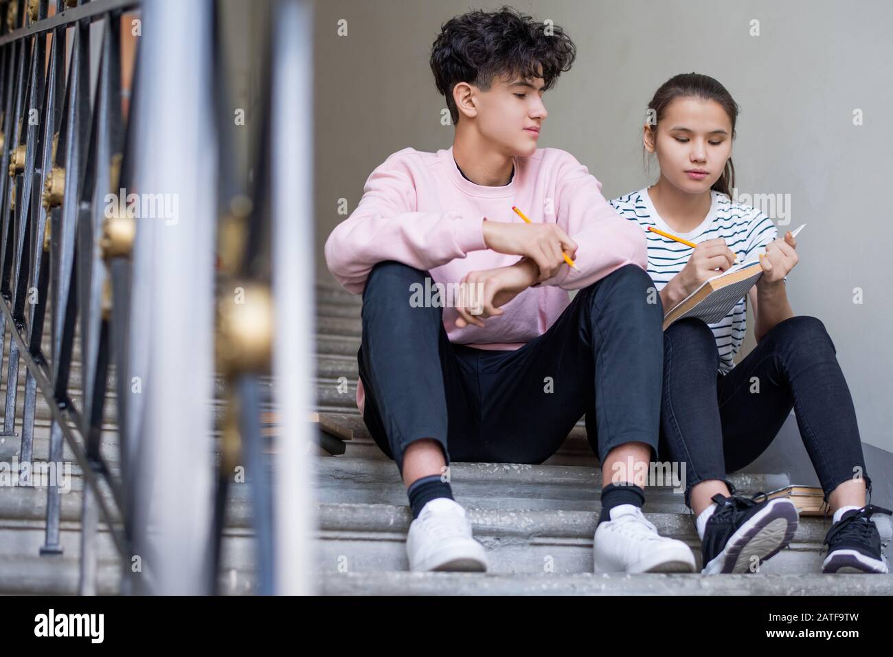 One of diligent learners making notes while both reading passage from book Stock Photo