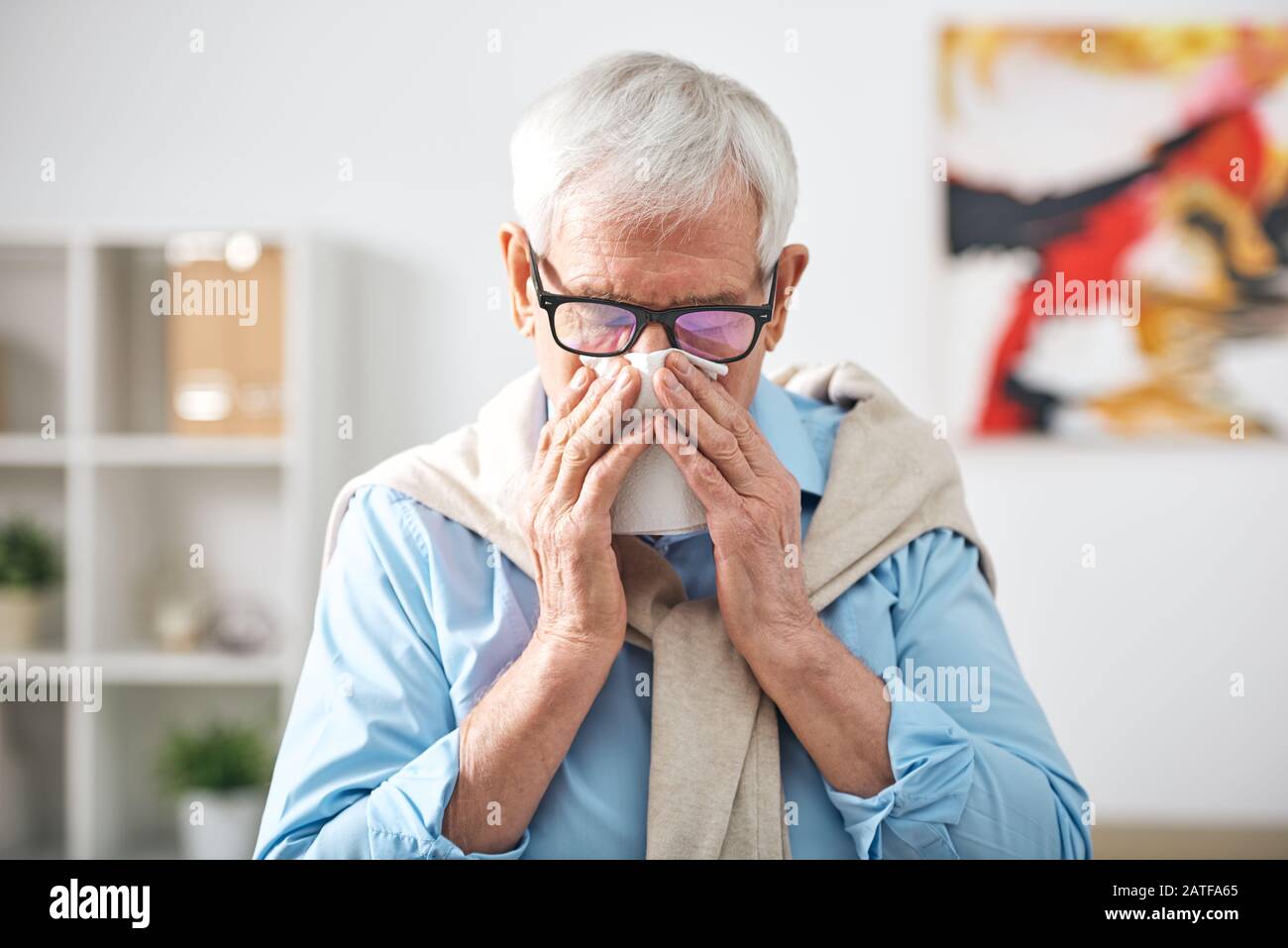 Sick senior retired man with handkerchief by his nose staying at home Stock Photo