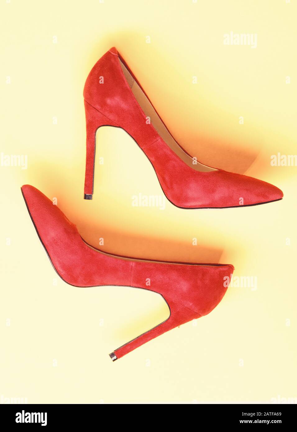 Luxury footwear concept. Footwear with thin high heels, stiletto shoes, top view. Shoes made out of red suede on yellow background. Pair of fashionable high heeled pump shoes. Stock Photo